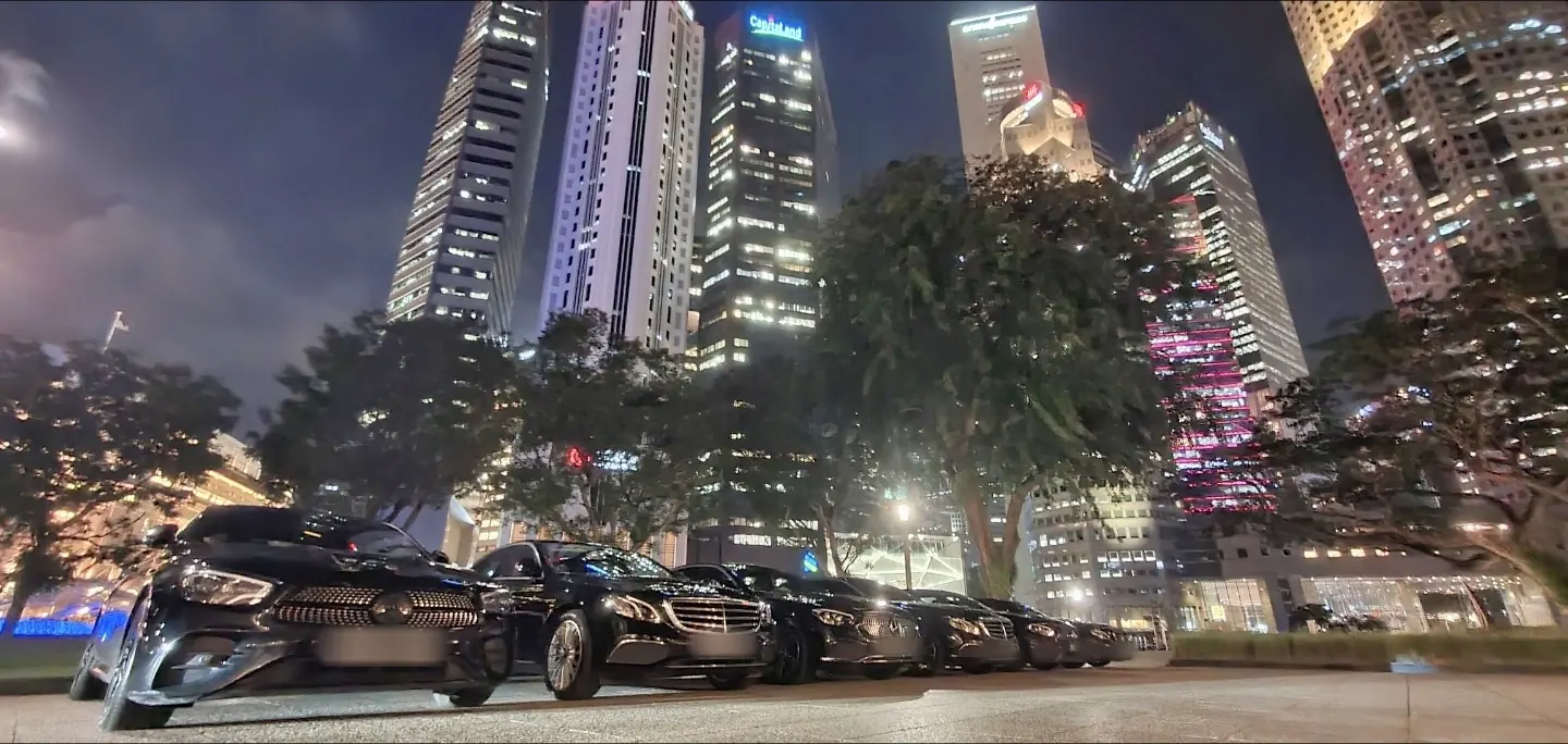 Line of black Mercedes-Benz E-Class sedans beneath the Singapore CBD skyline at night