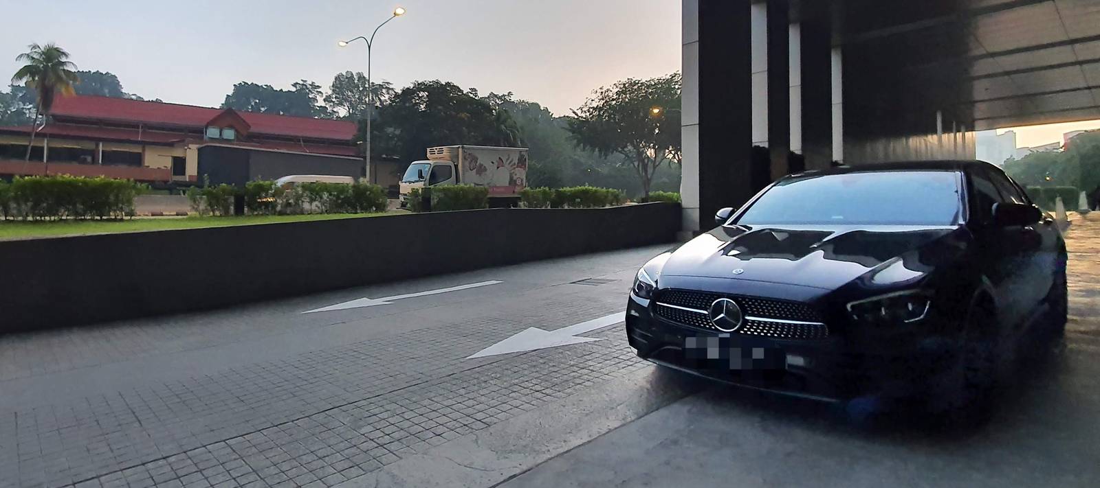 Black Mercedes-Benz sedan waiting at a hotel drop-off in Singapore at dusk